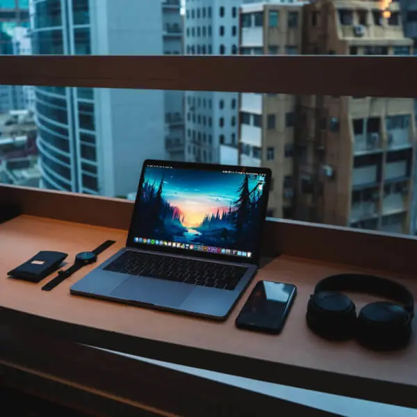 Laptop, mobile, headset and watch on working desk of freelancer Web Developer with view on buildings